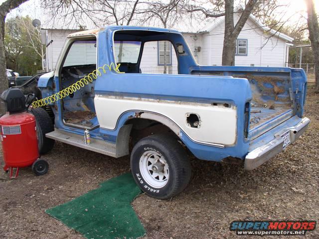 Blue and white Ford Bronco body with doors removed, sitting outside next to an air compressor