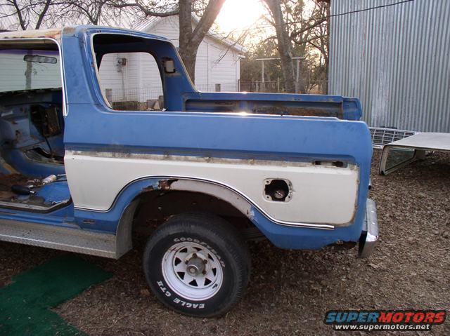 Rear quarter view of a blue and white 1978 Ford Bronco with a removed fuel door