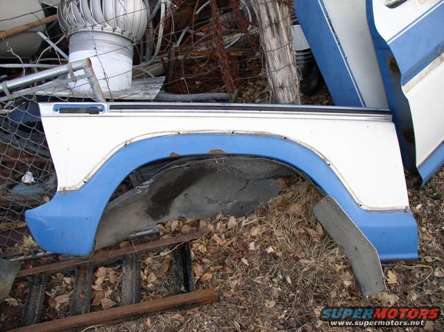 White and blue fender with rust, lying on the ground next to other scrap metal