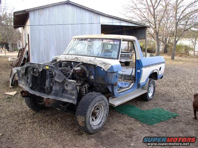 Blue and white pickup truck, front end removed, parked in a yard