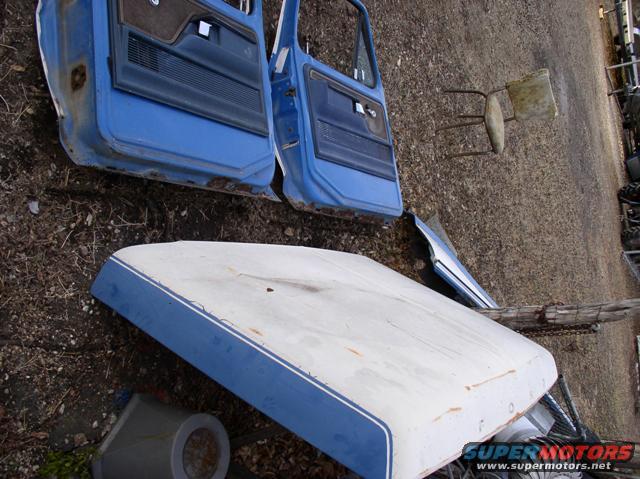 Two blue Ford Bronco doors and a white hood with blue trim, lying on the ground