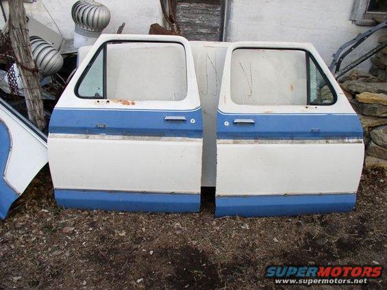 Two white and blue car doors with rust spots and visible door handles