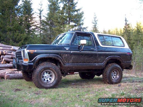 Black 1978 Ford Bronco with white removable top parked on grass near a pile of logs