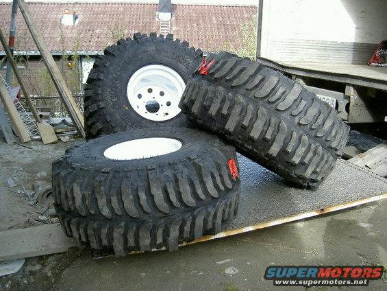 Three large off-road tires with white rims on a metal ramp