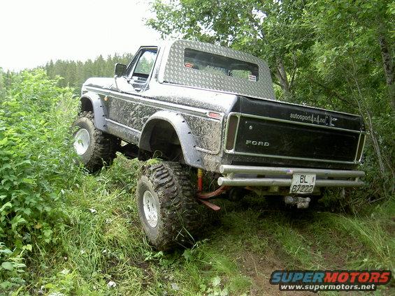 Muddy 1978 Ford Bronco with aftermarket bumpers and diamond plate bed cover driving off-road