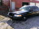 2001 Ford Crown Victoria - A black 2001 Ford Crown Victoria is parked in front of a red building.