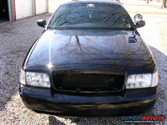 Front view of a black sedan with a skull sticker on the windshield. It's parked on a gravel driveway in front of a garage