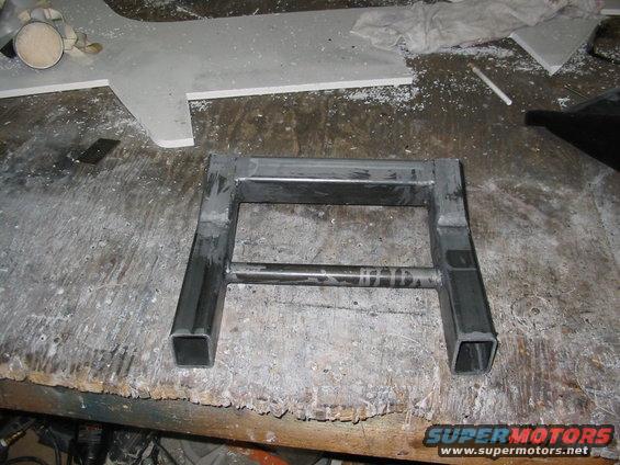 Metal frame with square tubing legs and a horizontal bar, resting on a cluttered workbench