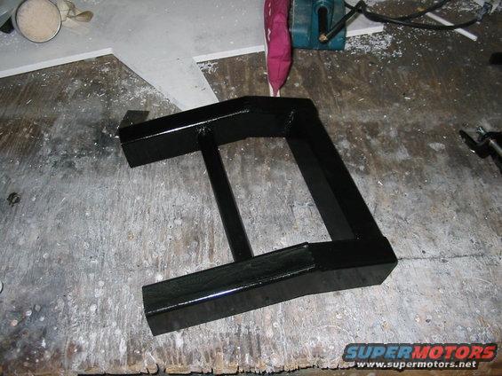 Black metal part on a workbench with Supermotors.net logo