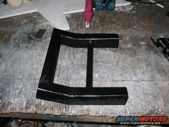 Black metal bracket with a central support bar, resting on a cluttered workbench