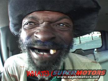 Man with a black hat and beard grimacing, inside a vehicle