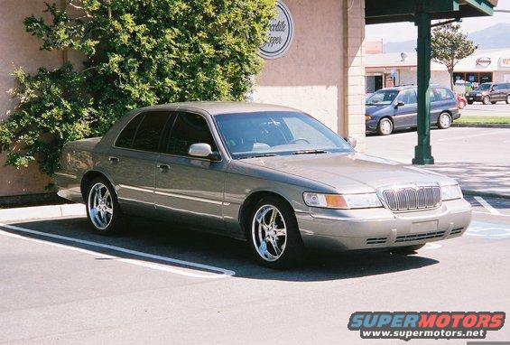 Gray 2000 Mercury Grand Marquis parked in a lot, chrome wheels, slight damage on front bumper