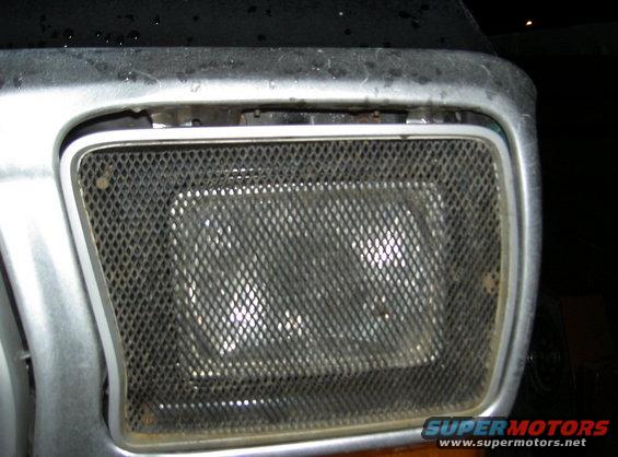 Close-up of a vehicle's headlight assembly covered by a diamond-patterned mesh grille