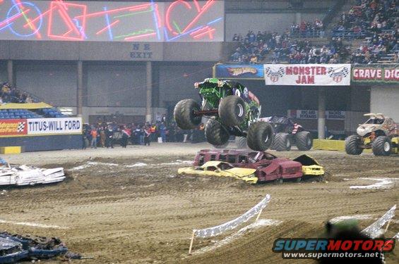 Monster truck in mid-air over crushed cars at an indoor event