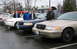 1999 Ford Crown Victoria - Several Ford Crown Victoria sedans are lined up in a parking lot with people standing next to them.