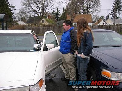 White and dark blue 1999 Ford Crown Victorias parked side-by-side, people between them