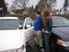 1999 Ford Crown Victoria - Two Ford Crown Victorias, a white one and a dark blue one, are parked next to each other with people standing between them.