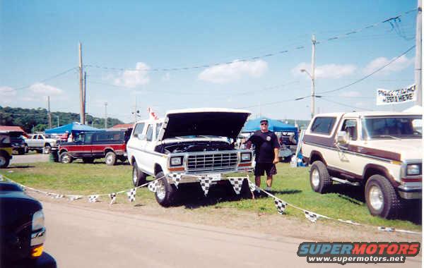 White 1978 Ford Bronco with hood open, man standing next to it. Another Bronco is parked to the right