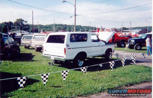 White 1978 Ford Bronco parked on grass with hood open, checkered flags in foreground