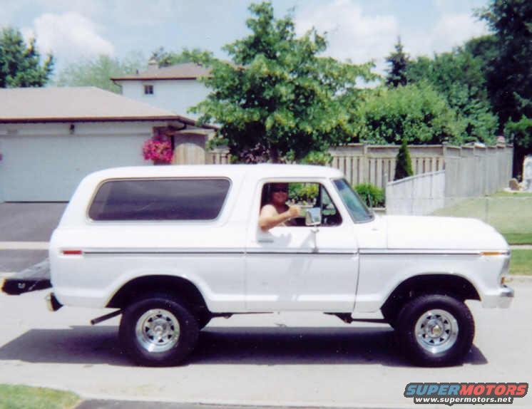 White 1978 Ford Bronco driving on a suburban street, side view