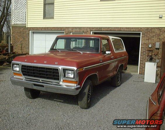 1978 Ford Bronco, red with white top, parked outside a garage