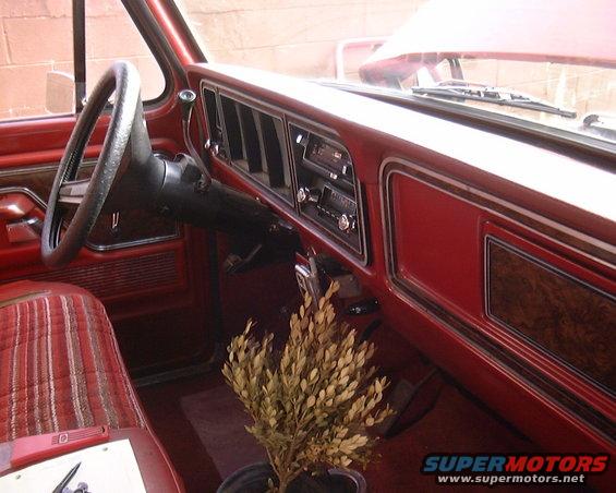 1978 Ford Bronco interior with red dashboard, wood trim, striped seats, and a plant