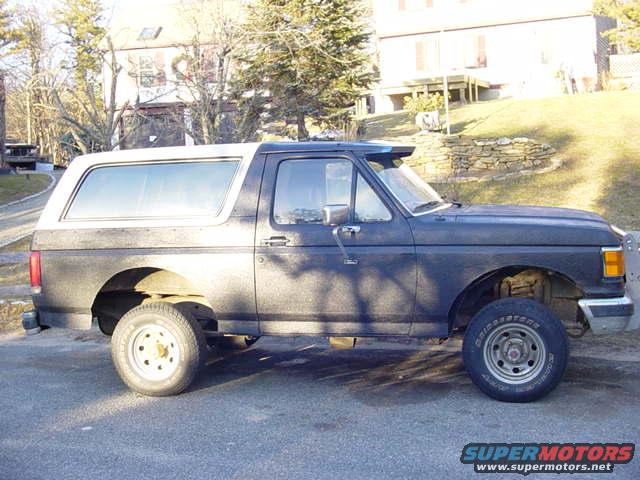 Side view of a dark blue 1989 Ford Bronco with a white camper shell