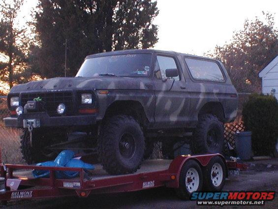 Camouflaged Ford Bronco on a red trailer, front winch visible