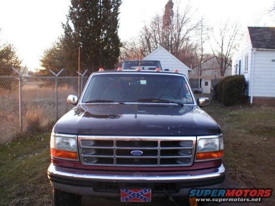 Front view of dark-colored Ford F-Series truck with a confederate flag license plate. Another truck is visible behind it