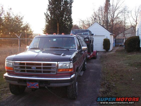 Dark red Ford F-Series truck front view towing a Jeep Cherokee on a trailer