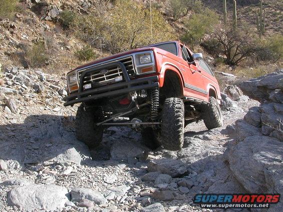 Orange Ford Bronco with aftermarket bumper and lift kit navigating a rocky desert trail