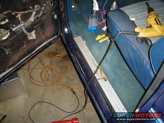 Blue car interior with exposed door panel wiring, tools, and a yellow drill on the seat