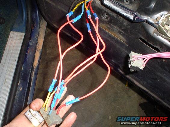 Close-up of a hand holding a wiring harness with blue connectors inside a vehicle