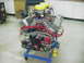 1990 Ford Mustang - A custom V8 engine assembly sits on a blue stand, prominent dual carburetors and red spark plug wires.