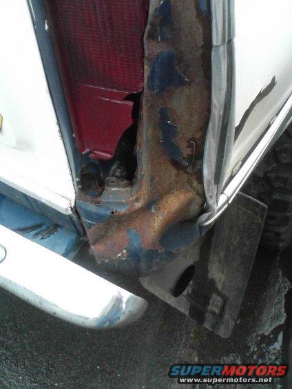 Close-up of heavily rusted and damaged rear corner of a vehicle, showing a broken taillight and exposed metal