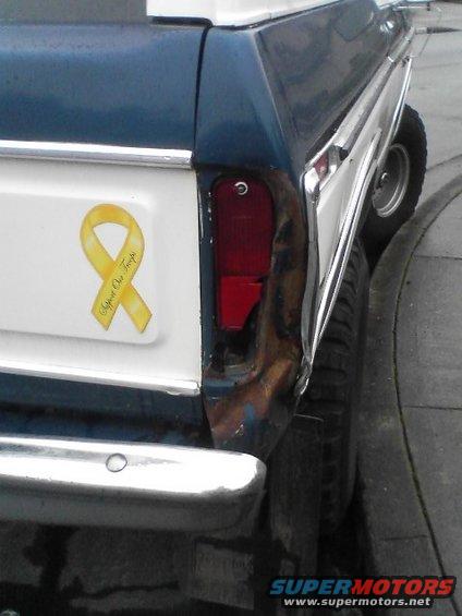 Rear corner of blue and white SUV with yellow ribbon sticker and damaged taillight