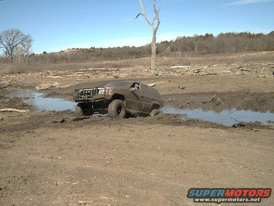 Dark green Jeep Grand Cherokee stuck in mud, front grille guard visible