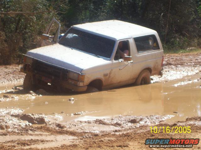 White 1989 Ford Bronco stuck in mud, driver's door open