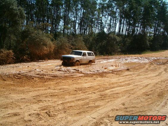 1989 Ford Bronco stuck in a muddy trail with trees in the background