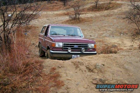 Maroon 1993 Ford Bronco navigating a dirt trail with front wheels partially sunk in sand