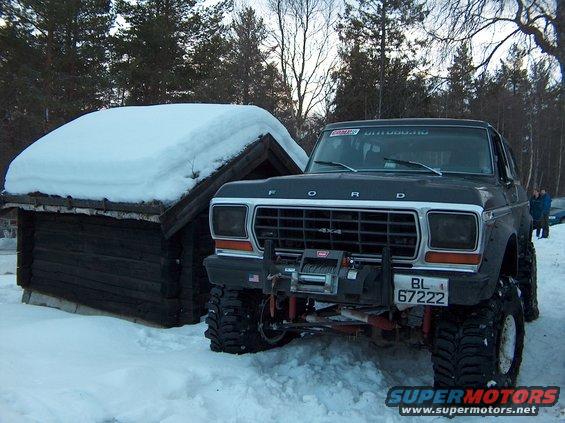 1979 Ford Bronco with winch and large tires parked in snow next to a wooden structure