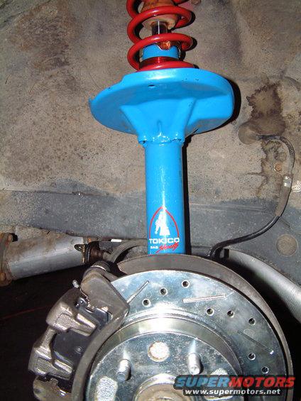 Tokico shock absorber with red spring and blue housing, part of a car's suspension system