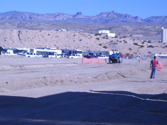 Blue off-road vehicle driving in a sandy area with RVs parked in the background and mountains beyond