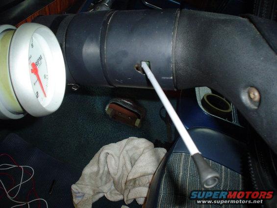 Vehicle interior with a tachometer, steering column, and floor mat. A white cloth lies on the floor