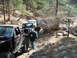 1993 Ford Bronco - A convoy of off-road vehicles, including a 1993 Ford Bronco, navigates a challenging rocky trail through a wooded area.
