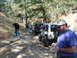 1993 Ford Bronco - A group of Jeeps are lined up on a dirt path surrounded by trees, with a man holding a camera in the foreground.