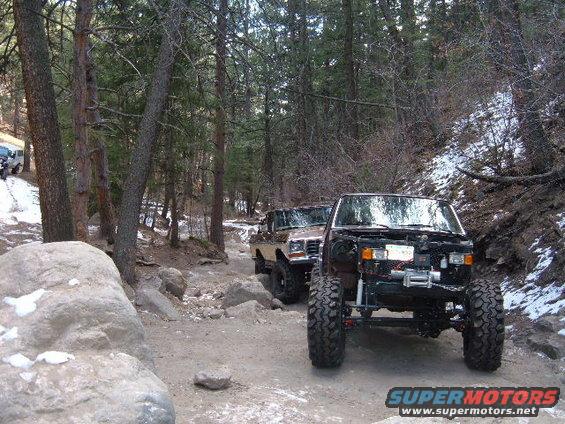 Two off-road vehicles on a dirt trail in a forest, one with its hood removed