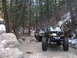 1993 Ford Bronco - Two modified off-road vehicles navigate a wooded trail with snow patches on the ground.