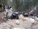 1993 Ford Bronco - Two off-road vehicles navigate a rocky, wooded trail with snow patches visible.