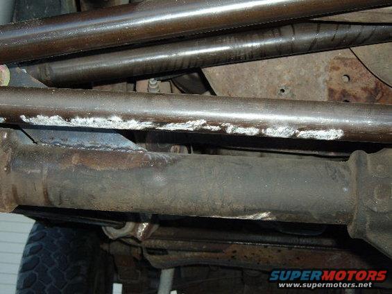 Underbody view of vehicle suspension and exhaust pipes with Supermotors.net logo